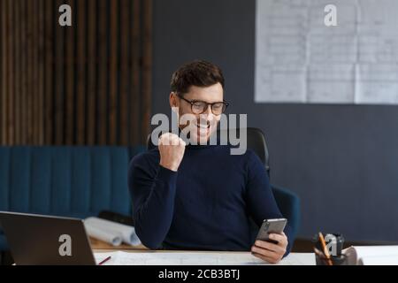 Young man using smartphone and smiling. Happy businessman using mobile phone apps, texting message, browsing internet, looking at smartphone. Concept Stock Photo