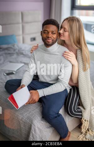 Smiling romantic multiethnic couple spending together cold weekend at home, enjoying each other, reading together the same book Stock Photo