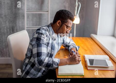 handsome serious African guy making notes in the bedroom, close up side view photo. free , spare time, talented young writer making up a poem Stock Photo