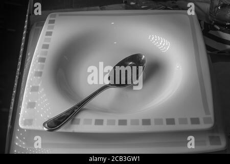 A lone soup bowl in black & white with contrast and single spoon providing contrast. Good mood and lighting Stock Photo