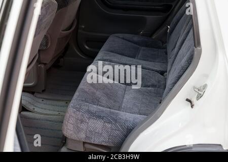 An open rear door of a white Japanese SUV overlooking a passenger row of seats made of gray textile material after dry cleaning before preparation for Stock Photo