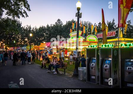 Tourists and locals enjoy the annual Pig Out in the Park in Riverfront Park, Spokane Washington, as they eat at food stalls and vendors as night falls Stock Photo