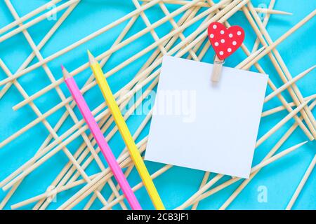 Notepaper holding by clothes pin with heart, pencils on a abstract blue background Stock Photo