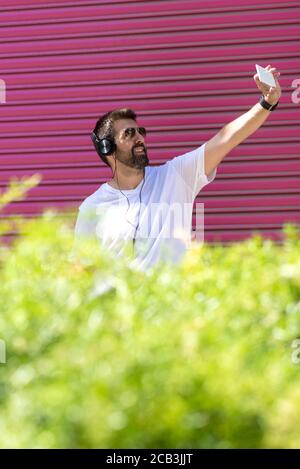 Bearded guy with sunglasses taking a selfie against pink wall Stock Photo