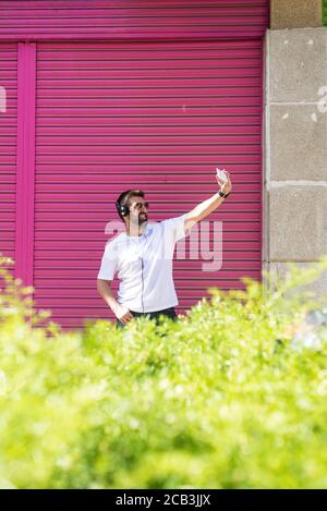 Bearded guy with sunglasses taking a selfie against pink wall Stock Photo