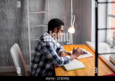 Attractive Afro student sitting at the table and preparing for exams, close up side view photo. education, Stock Photo
