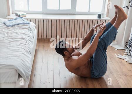 sporty man doing abs workout. ,Training indoors, young attractive muscular man doing morning exercise in the bedrooom, spare time, side view full leng Stock Photo