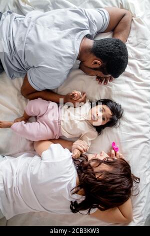 tired parents sleeping on the bed while their kid waking up, top view photo. family life Stock Photo