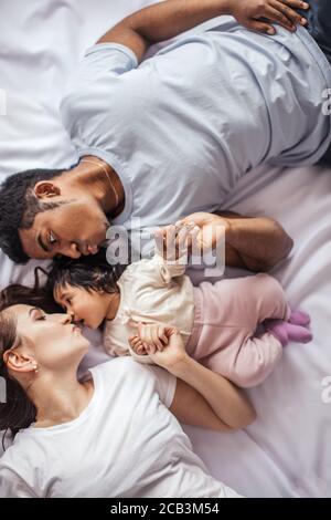 woman kissing her little child while lying on the bed with husband, top view photo Stock Photo