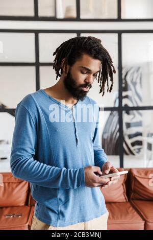 Serious young african man using mobile phone while standing in the appartment Stock Photo