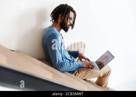 Handsome young african man sitting on a staircase at home, using laptop computer Stock Photo