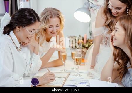 cheerful smiling group of young caucasian and beautiful models gathered in salon to listen to, get consultation and try on new wedding dresses made by Stock Photo