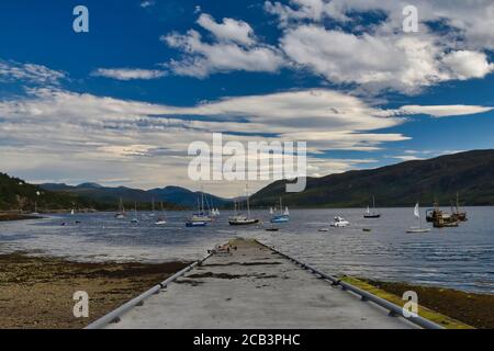 Ullapool jetty, sea, sailing boats and mountains in Scottish Highlands on North Coast 500 route on sunny summer day with blue sky and clouds Stock Photo