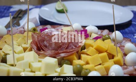 Dishes with quail eggs various types of cheese salami turkey meat green olives sticks to serve and white dish with lemon out of focus on blue Stock Photo