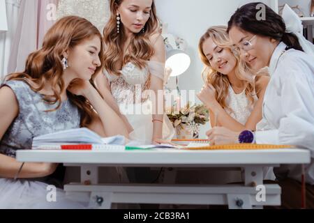 caucasian group of women gathered together in designer's office to discuss new style of dress, young girls in trendy white wedding dresses Stock Photo