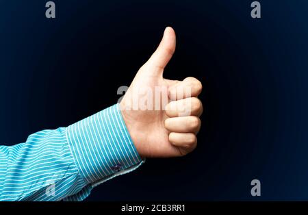 A young man' hand is displaying a thumbs up, indicating that he likes or approves of something on dark background Stock Photo