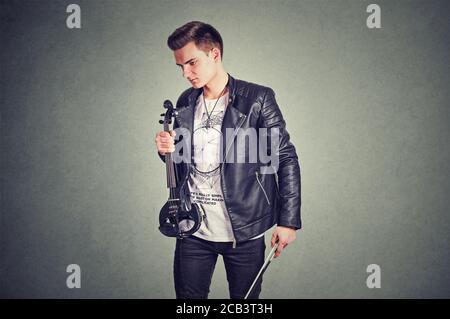 Music passion, hobby concept. Young sad disappointed man looking down holding electronic violin in studio on gray wall background. Horizontal shot mod Stock Photo