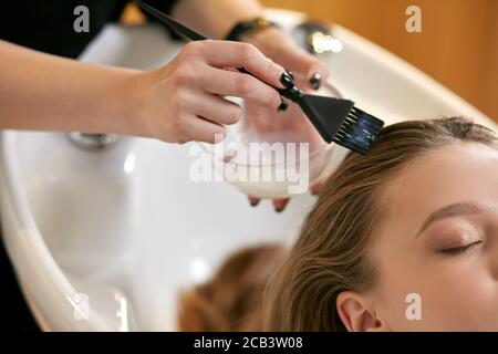 close up of young caucasian female hairdressed hands dyeing long hair to beautiful girl. Getting beauty procedures. Stock Photo