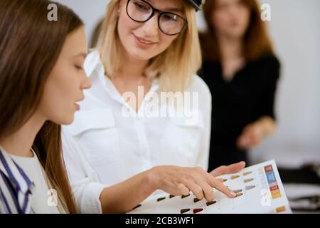 stylish modern blond hairdresser hold colour palette in hands and show, advice to young client which colour is appropriate for her face, isolated in b Stock Photo