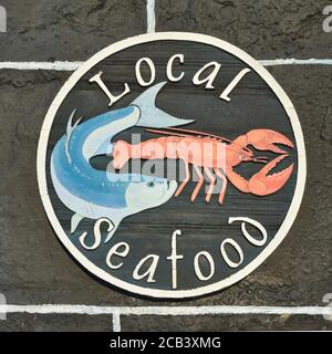 Local seafood sign with blue fish and orange lobster illustration, on rustic black and white wall outside Plockton Hotel, Scottish Highlands Stock Photo