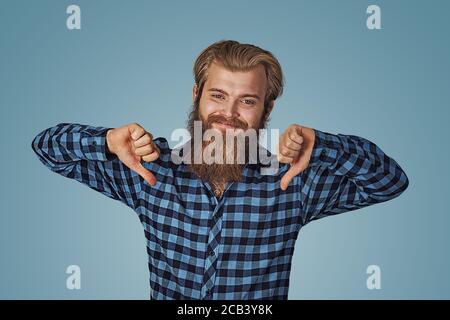 Smiling man with thumb down. Cheerful guy expressing disapproval. Dislike concept.  Hipster male with beard in blue plaid checkered shirt showing thum Stock Photo