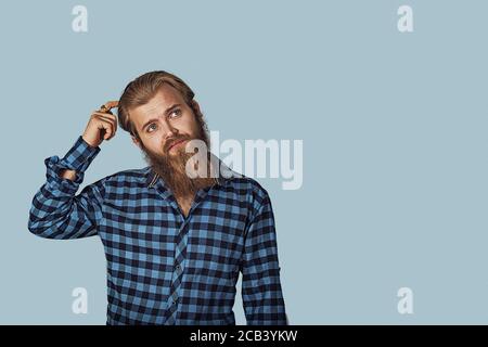 Thinking perplexed man looking up. Thoughtful guy scratching head solving a problem. Hipster male with beard in blue plaid checkered shirt. Isolated o Stock Photo