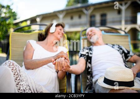 Senior couple with headphones outdoors on holiday, relaxing. Stock Photo