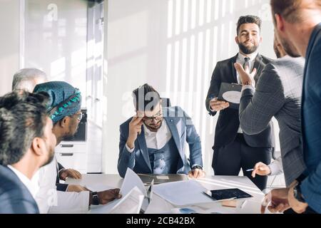 Conflict on business meeting with team. Young male Chief Executive feeling tired, stressed and exhausted during stressful business negotiations with i Stock Photo