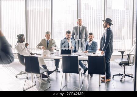 Elegant well-dressed business men of different age and ethnicity in suits gathered together for negotiating, collaborating in spacious modern office m Stock Photo