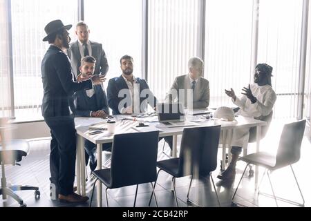 Elegant well-dressed business men of different age and ethnicity in suits gathered together for negotiating, collaborating in spacious modern office m Stock Photo