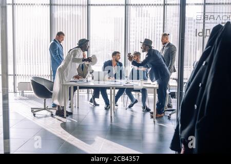 Two young Indian and Arabian business partners interacting, argue passionately, having positive mood, standing opposite each other in office with big Stock Photo