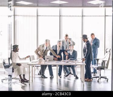 Hot debates. Group of interracial business partners disagree with company CEO, dressed as Arab, people have dispute, using lots of hand gestures, but Stock Photo