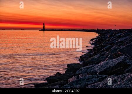 The sun is setting behind the lighthouse of the suburb Hohe Düne Stock Photo