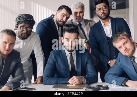 Multicultural business people including Arabic, Caucasian, Indian, Hispanic standing in modern office in group and looking confidently at camera. Conc Stock Photo