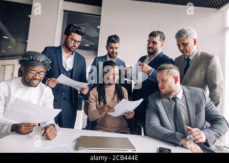 Happy satisfied business men of different race and age, dressed in formalwear together with young African woman applauding to the camera after visitin Stock Photo