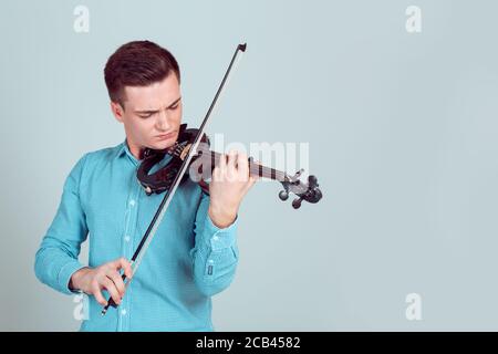 Man in shirt playing modern violin instrument sanding on light background Stock Photo
