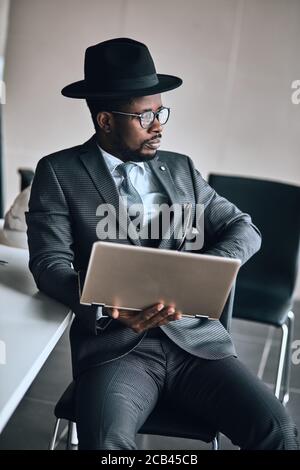 gorgeous boss is resting with laptop. good looking fashion guy in grey suit spending time in front of the laptop. close up portrait Stock Photo