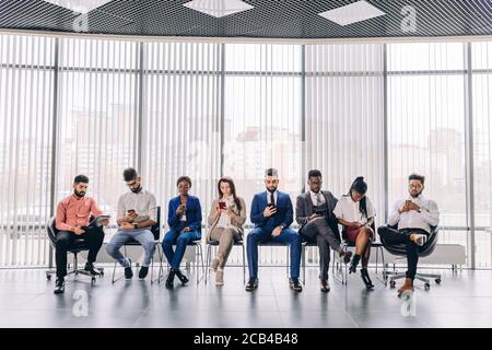 diverse attractive young people in stylish fashion clothes are sitting on the chairs and using mobile phones Global communication concept. Stock Photo