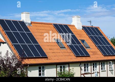 Modern black solar panels on the red tile roof of an old house with blue sky background. Stock Photo