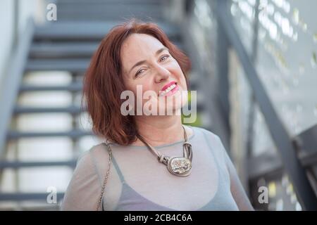 Portrait of elegant middle-aged woman smiling at camera posing on street Stock Photo