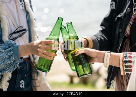Close-up of unrecognizable girls standing in circle and clinking beer bottles outdoors Stock Photo