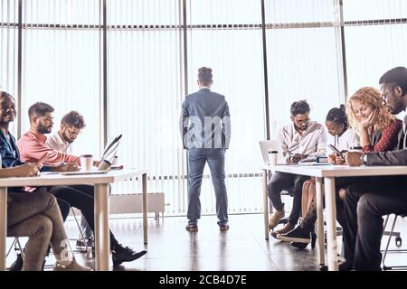 Successful team leader is making up a plan while his colleagues are concentrated on work. boss is looking through the window while his employees are s Stock Photo