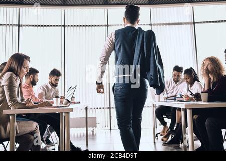 elegant smart man is entering a room with hardworking office people. job interview.lazy man is walking in the office Stock Photo