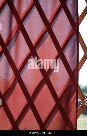Red wavy natural fabric curtain over wooden partition made of bamboo slats, natural oriental decor Stock Photo