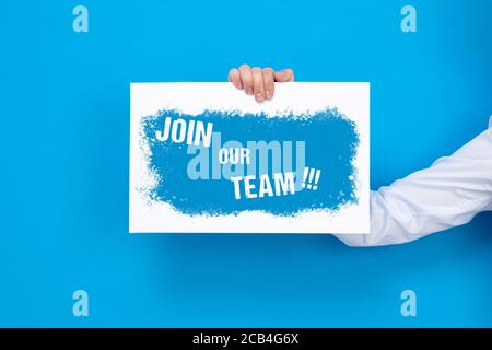 Hand holds white board with Join our team sign on blue background. Stock Photo