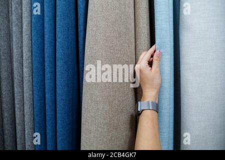 Young woman choosing fabric for new curtains in a store. Samples of the curtain hang on hangers on a rail in the store. Samples of textures of fabric Stock Photo