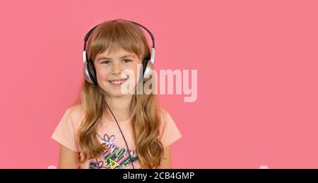 Little girl in headphones, cheerfully listens to her favorite song. A girl on a pink background listens to music. The child develops a taste for music. Beautiful little girl cheerfully smiles on a pink background. Stock Photo