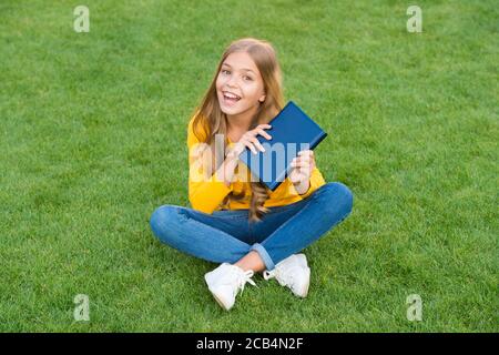 Girl reading book outdoors green lawn background, intellectual hobby concept. Stock Photo