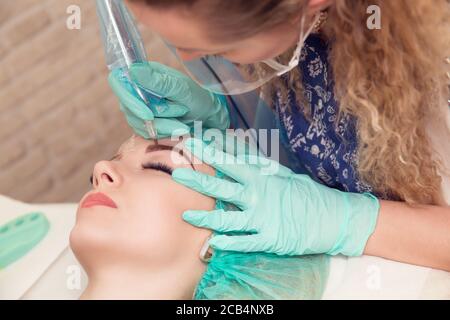 Micro pigmentation eyebrows work flow in a beauty salon. Woman having her eye brows tinted. Semi-permanent makeup for eyebrows. Focus on model's face Stock Photo