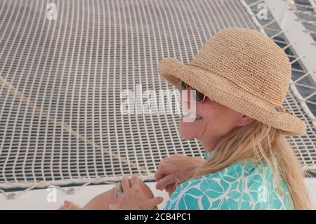 Happy outside. 60-year old active senior mature woman in straw hat on a boat smiling with big smile and white teeth. Happy retirement. Model release. Stock Photo